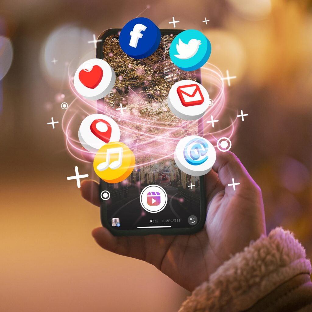 A hand holding a smartphone with various social media icons (Facebook, Twitter, Email, Location, Music, Heart, and Reel) floating above it, connected by swirling lines of light. The image represents Webbdesignz's comprehensive social media management services, enhancing connectivity and engagement across platforms.